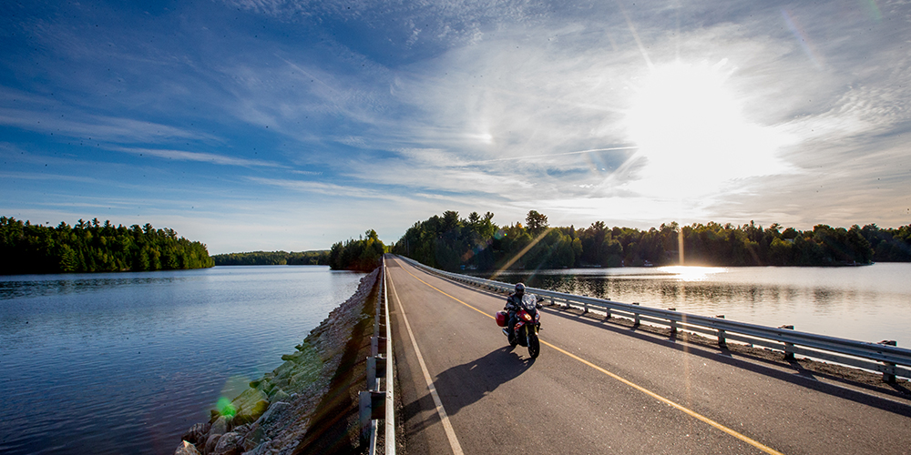 A long motorcycle speeds down a highway surrounded by beautiful blue water on a sunny day