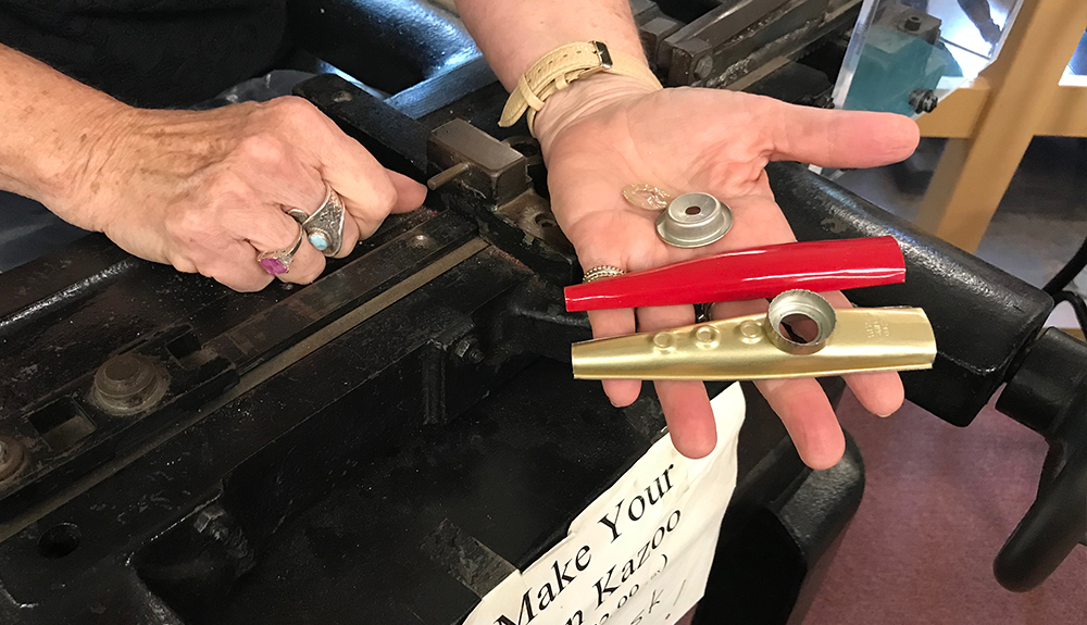 Hand holding out deconstructed pieces of a gold and red kazoo