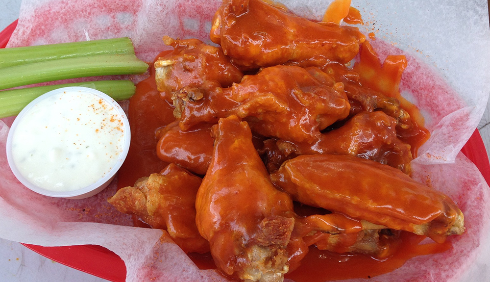 Plate of saucy Buffalo wings with a side of celery and ranch dip