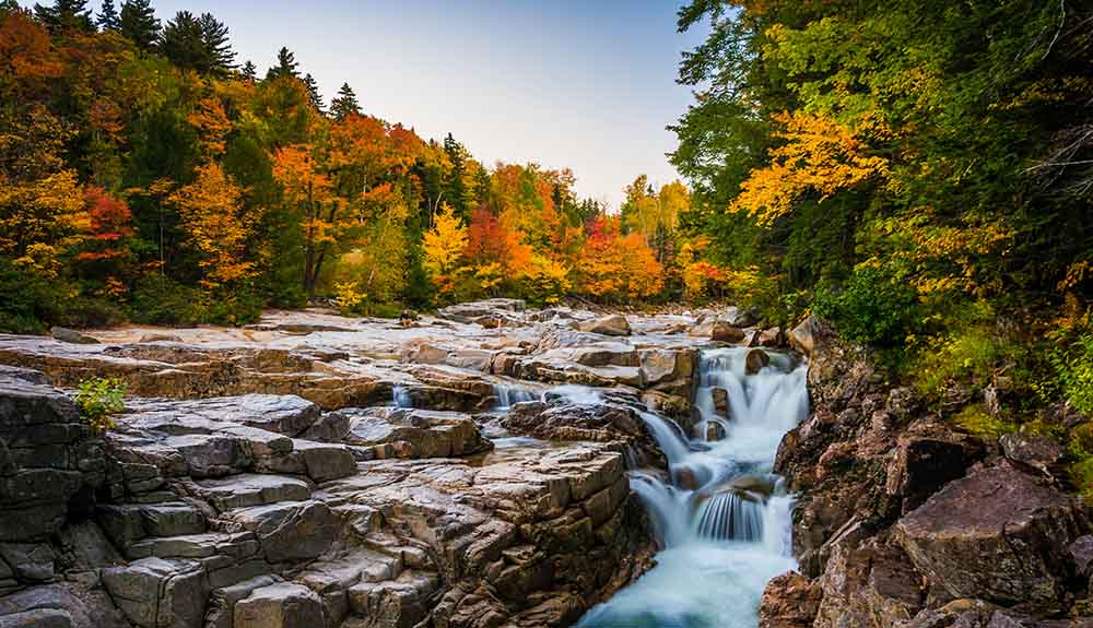 Small rocky waterfall in a lovely wooded area on a fall day, orange and red leaves seen on the trees