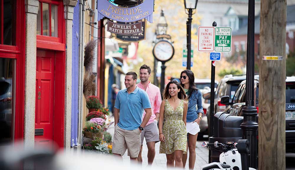 Four young adults in summery clothing happily strolling down a shopping street in New Hampshire