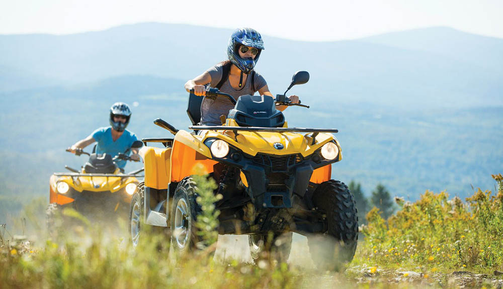 Two people race down dusty trail on yellow RVs on mountainous field in New Hampshire