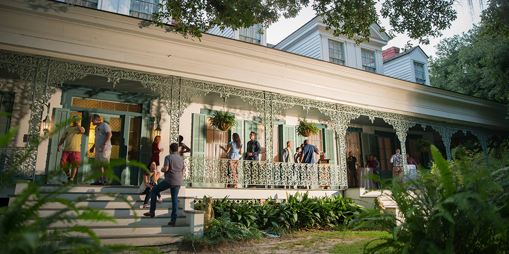 Tourists milling around the porch of a historic building with classic Southern architecture