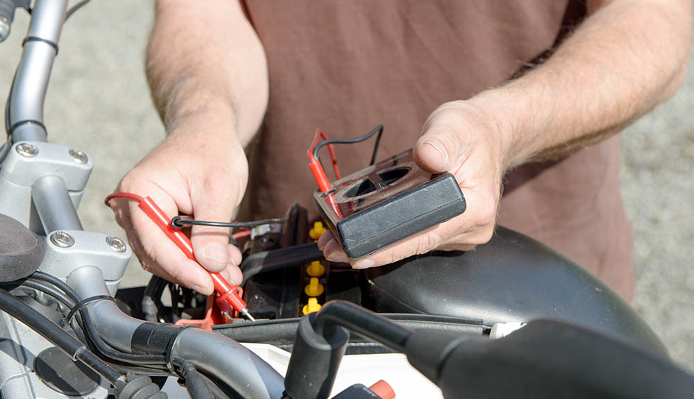 A person's hands are seen checking a motorcycle battery