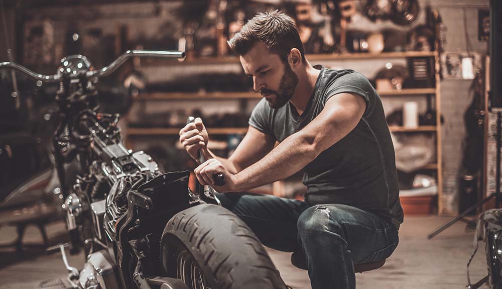 A young bearded man works on a motorcycle in a dimly lit garage