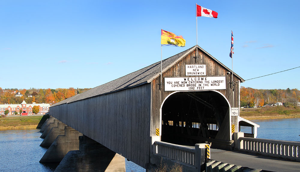 Hartland covered bridge, a wooden covered bridge with welcome sign and Canadian and New Brunswick flags proudly displayed