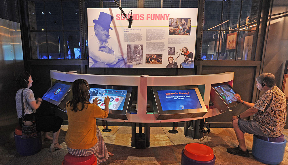 A family enjoying the National Comedy Centre, sitting at an information station and reading, looking at pictures of comedy history