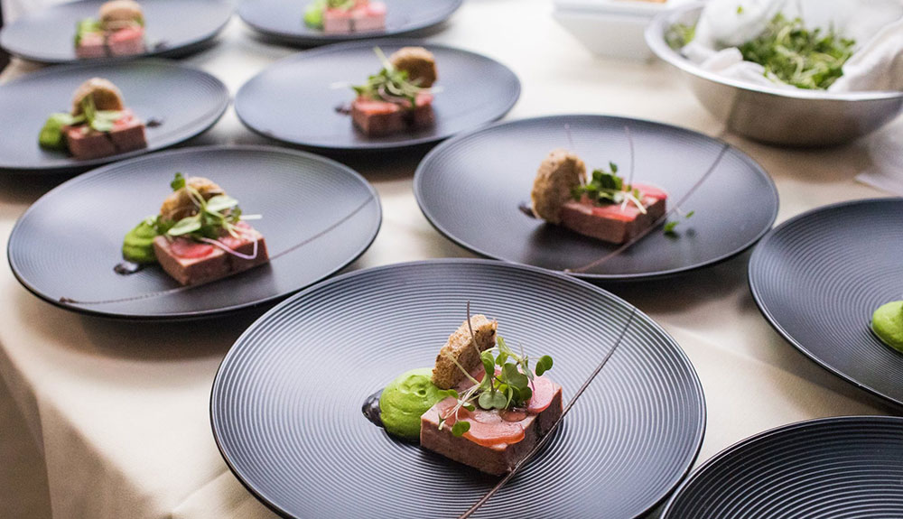 Graphic black plates with elegantly plated appetizer comprised of toast with salmon, fresh herbs and a pesto sauce