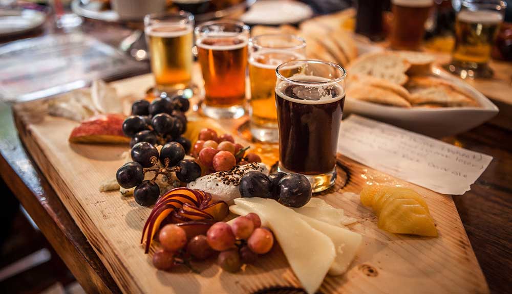 A flight of beers are shown on a board with cheese and grapes