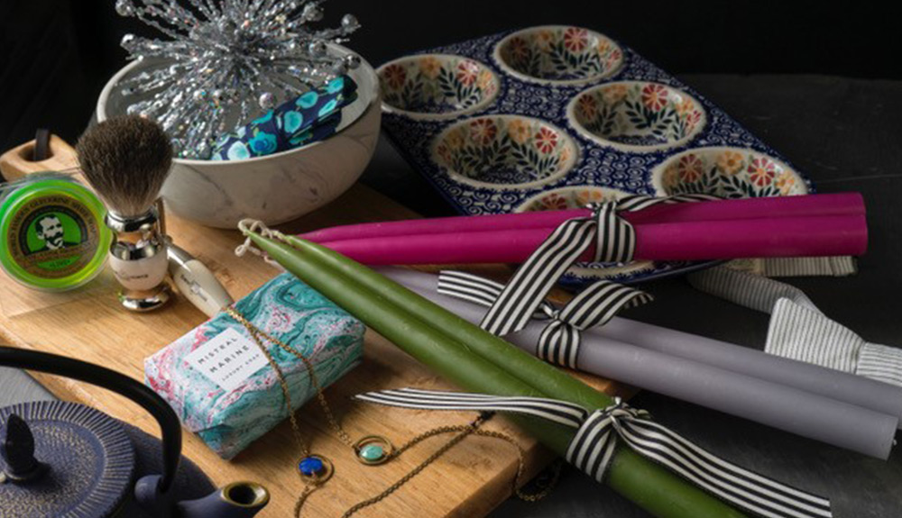 Green, grey and pink candles are tied in bundles of two with ribbon and various gift wrapping and holiday decors on the table nearby