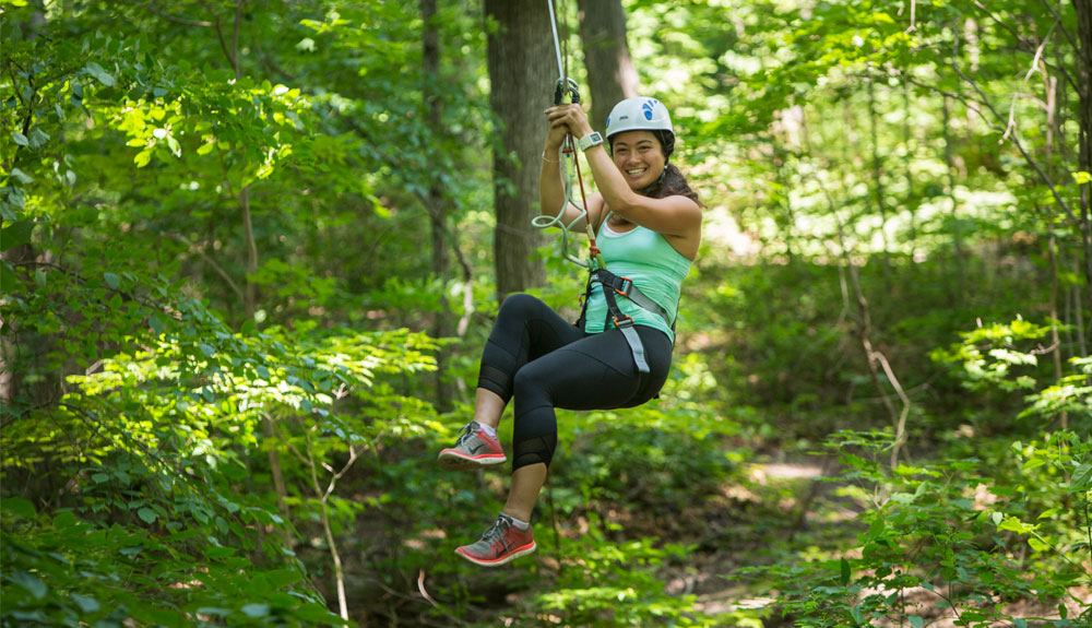 A woman is shown zip lining through a forest