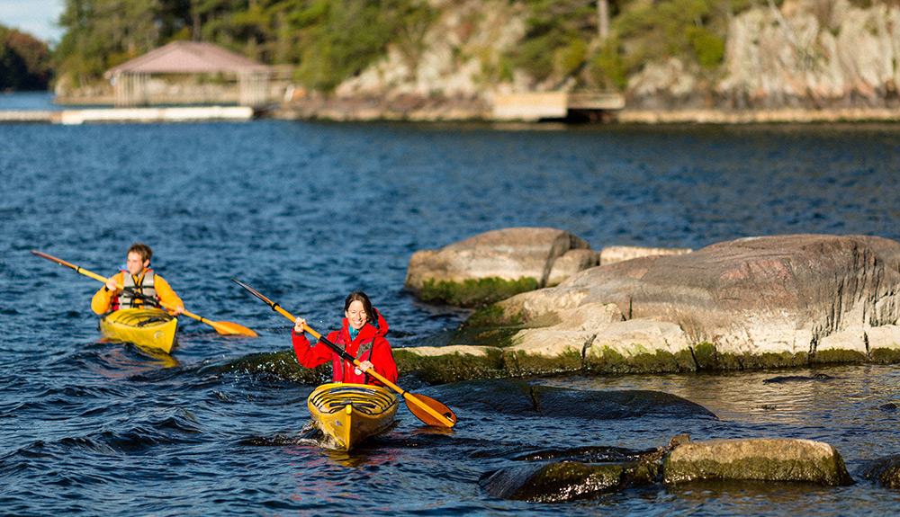 Two kayakers paddle past rocks on a lake in the 1000 Islands, Ontario
