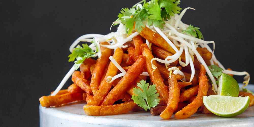 Close up shot of pad Thai fries garnished with bean sprouts and cilantro with a side of lime wedges 
