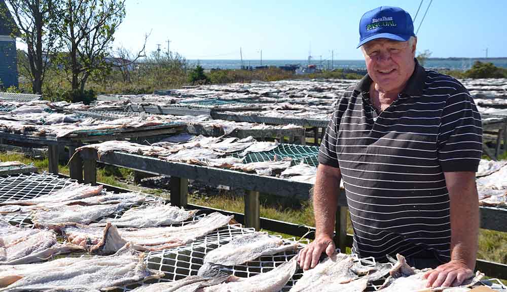 An older man smiles in front of rows of dried fish