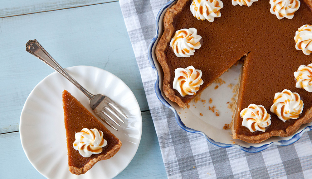 A beautiful pumpkin pie with small dollops of whipped scream, one slice cut out and ready to be enjoyed on a plate