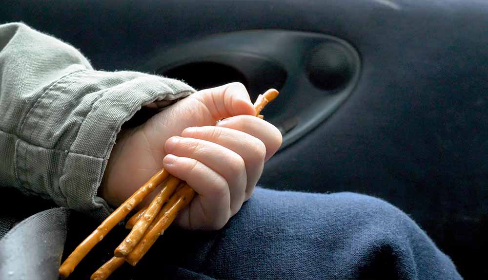 A child's hand is shown holding pretzel sticks in a car