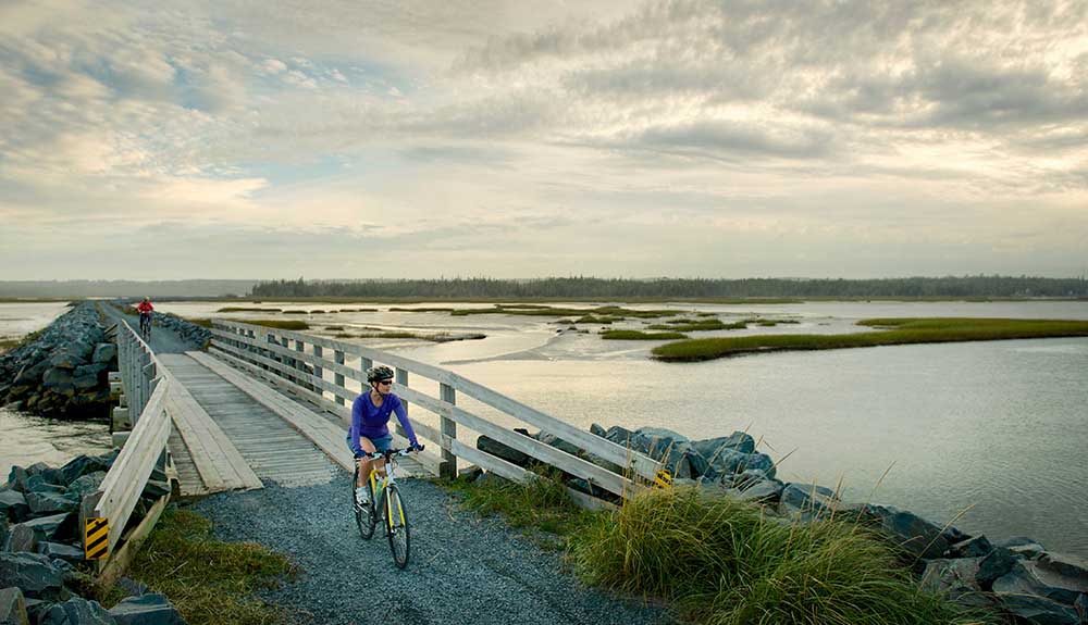Cyclist with helment on crosses wooden bridge that stretches across the water