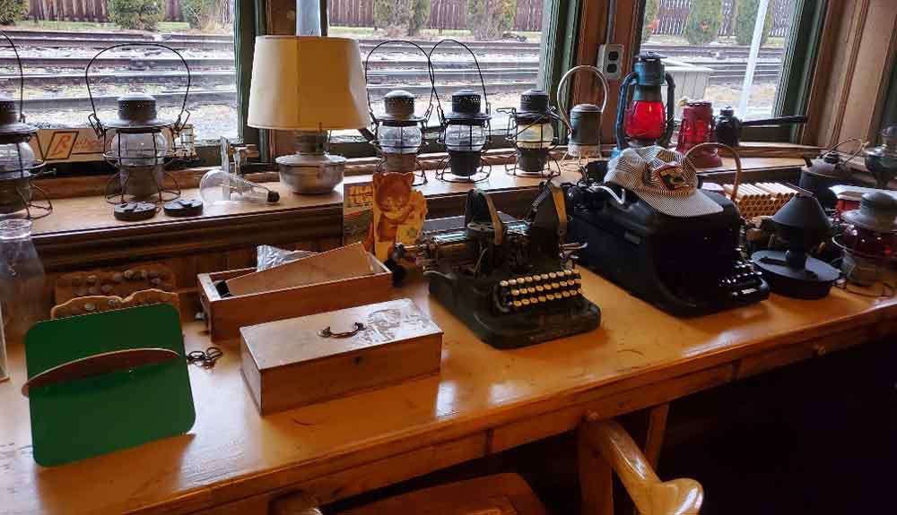 At the Grand Trunk Railway station, there is a table that displays old lanterns, a black typewriter, and other artifacts.