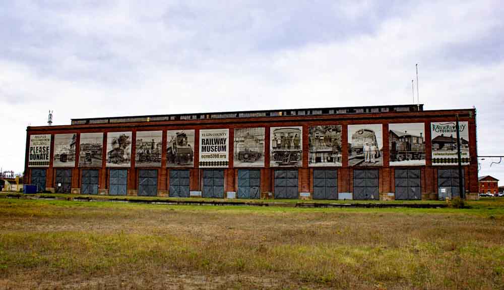 A long building with a sign in the middle that says Elgin County Railway Museum. On both sides of it are large black and white photos of older locomotives.