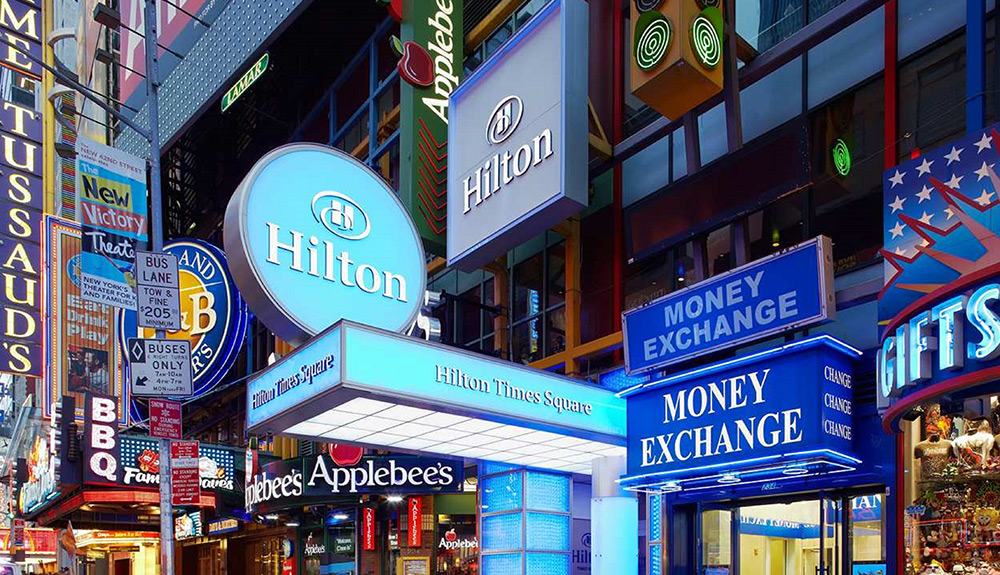 Hilton Time Square entrance between an Applebee's restaurant and Money Exchange store front in New York City 