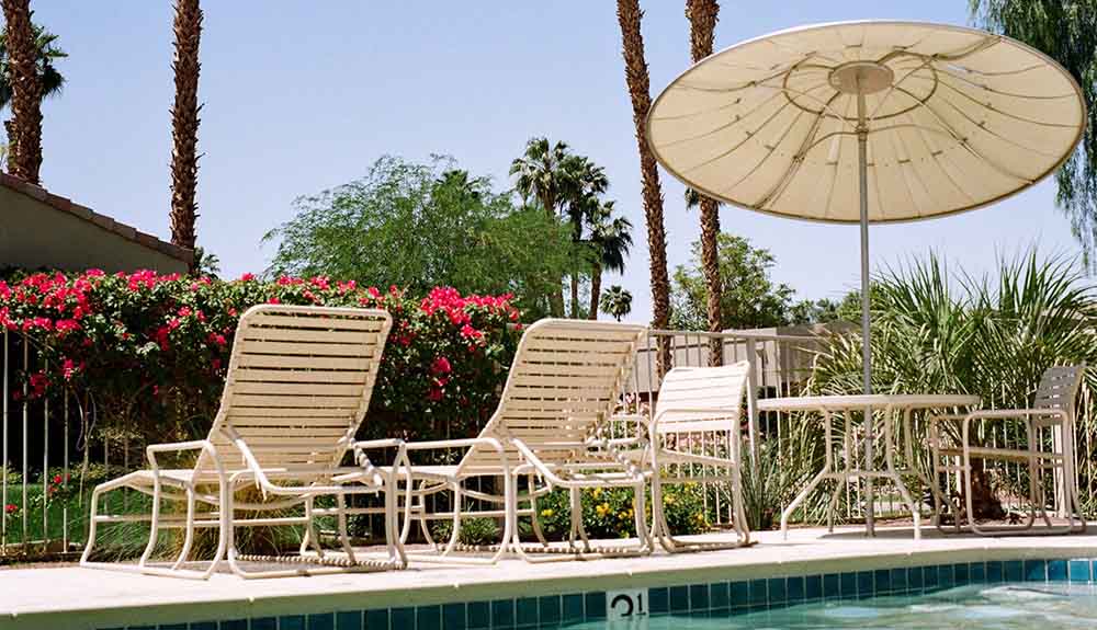 Pool lounge chairs and a table shaded by an umbrella at the edge of a pool
