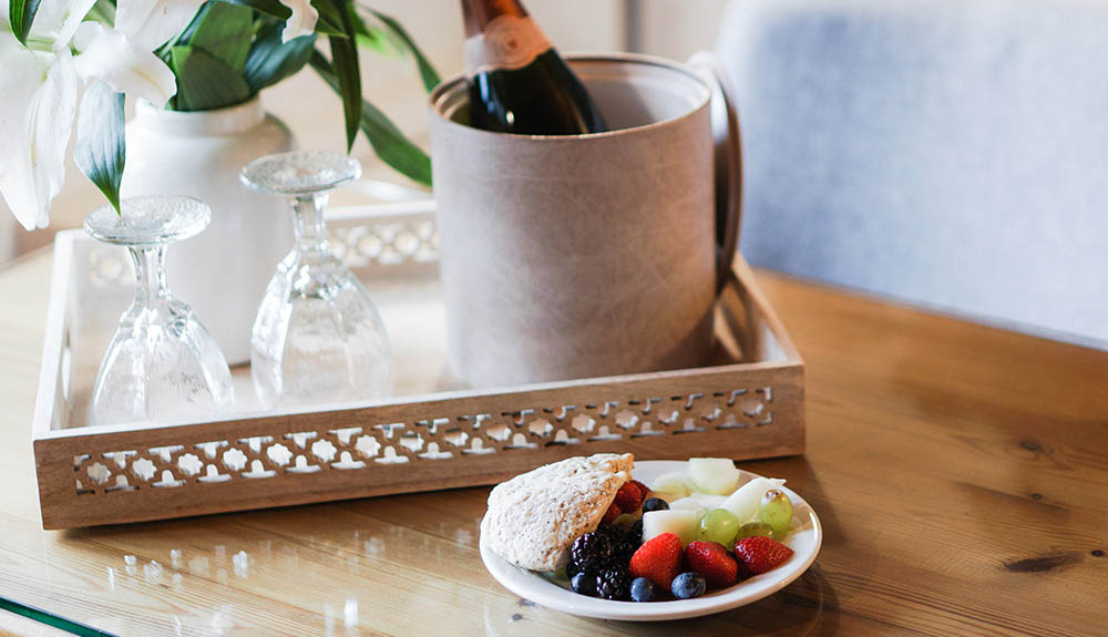 Hotel breakfast laid out on table with plate of fresh fruit and ice bucket with champagne, empty glasses at the ready