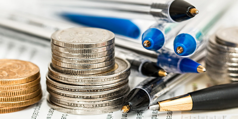 A stack of Canadian loonies, toonies and quarters and a stack of pens sit on a sheet of paper