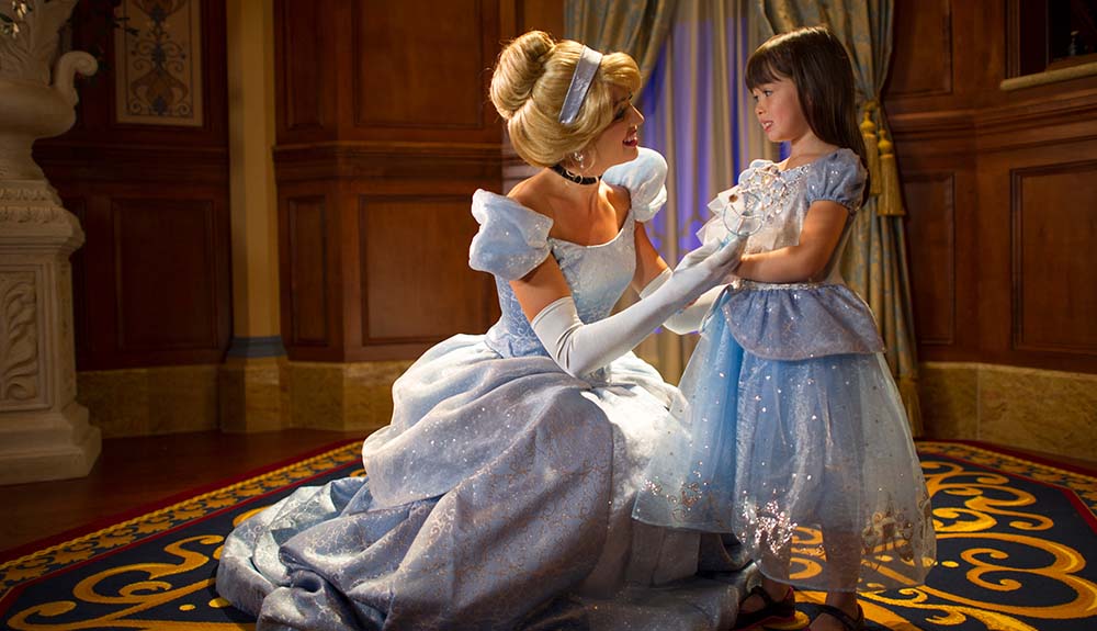 Woman dressed as Cinderella elegantly squatted down as she talks to a little girl wearing a princess dress