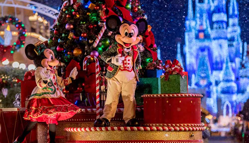 Micky and Minnie Mouse dressed for the holidays in front of a Christmas tree while on a float during a parade