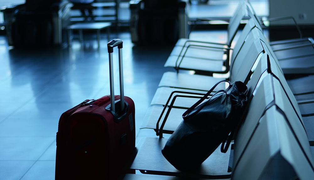 Airport lounge with carry-on bag on wheels standing in front of a seat with a purse on it