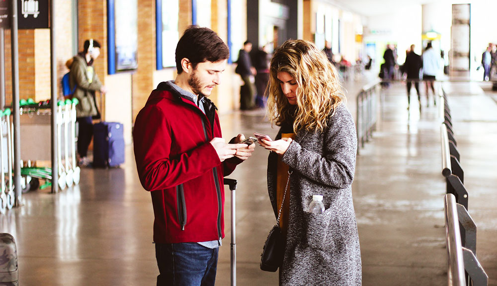 Man and woman in the airport checking their phones