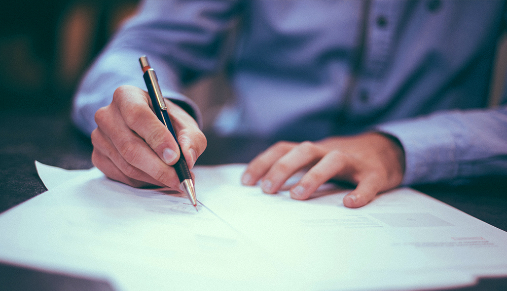 Man in a button up writes on paper with a ballpoint pen
