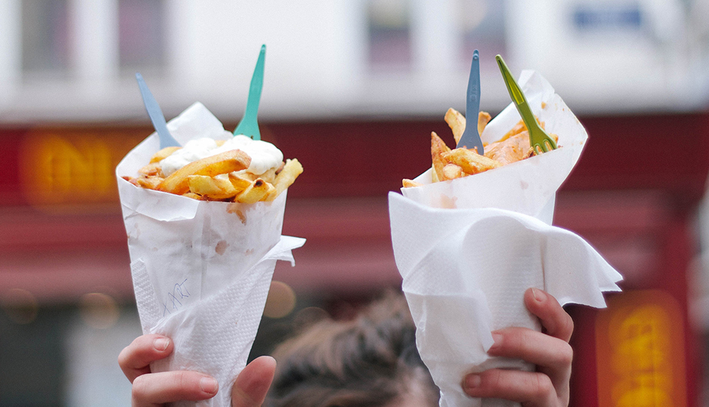Someone holding up two paper cones filled with fries and colourful mini forks sticking out on top