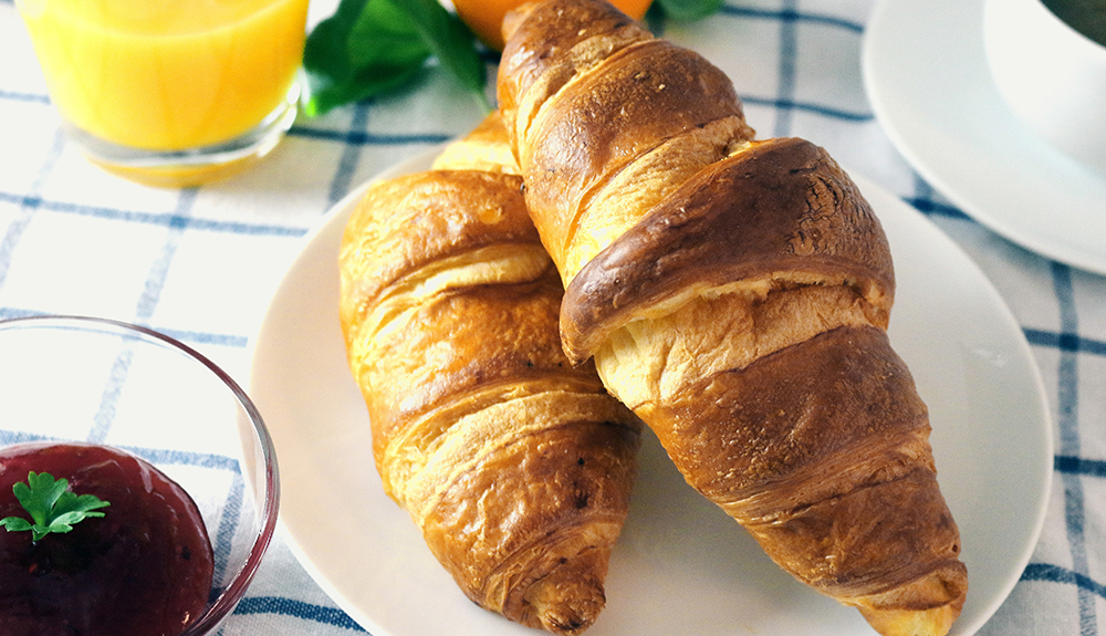 two fresh buttery croissants on a white plate
