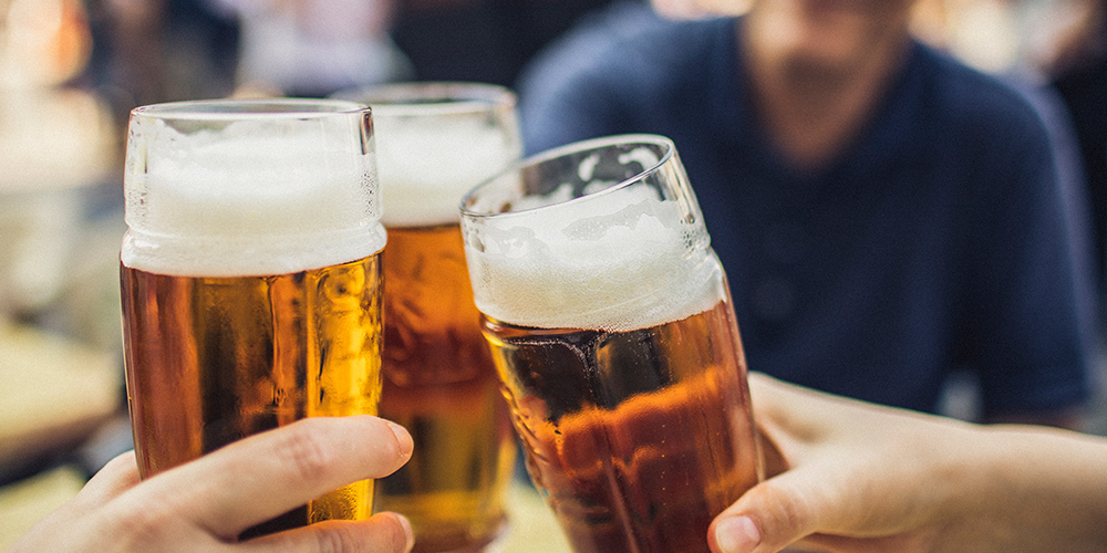 Three pints of beer held by different hands in the midst of a cheers