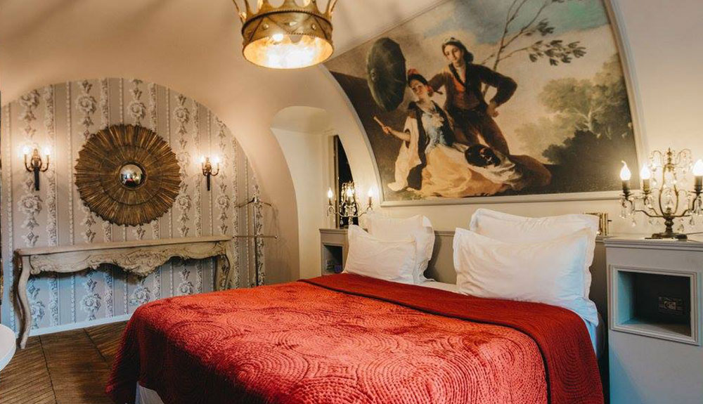 Large bed with a red comforter and a European painting above the headboard in Paris