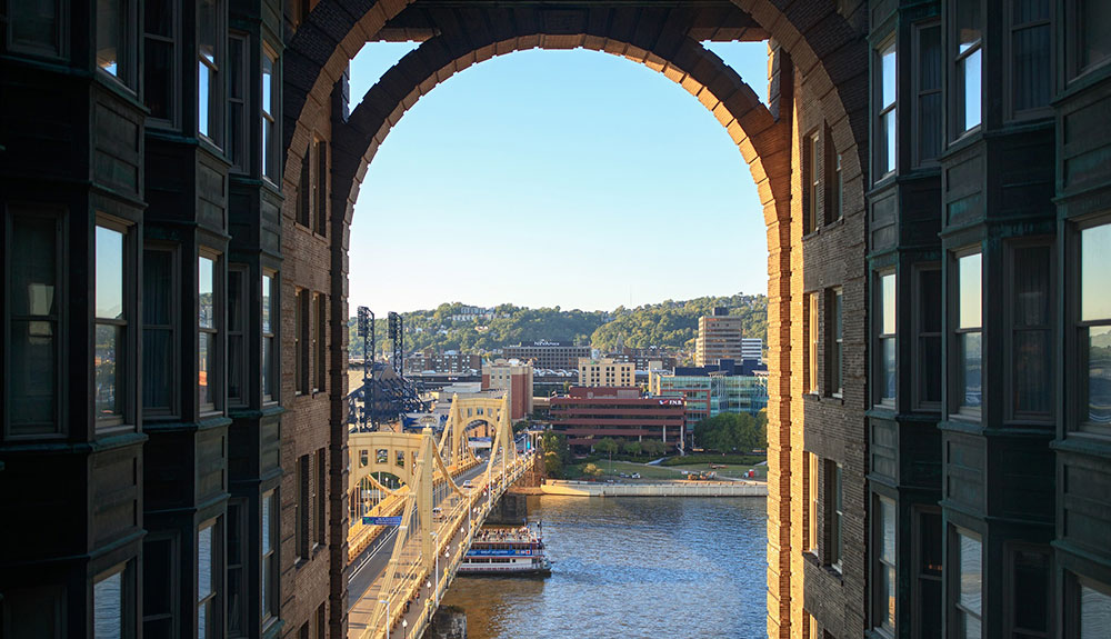 A view through an archway of the Renaissance hotel shows a bridge over a river and buildings on the other side