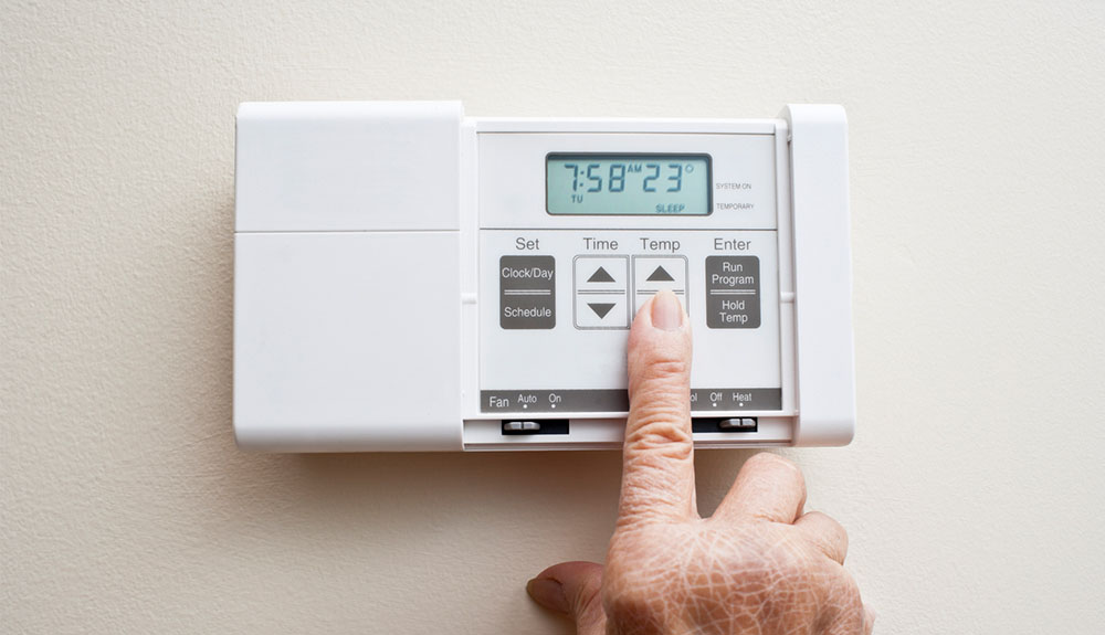 Person lowering the heat on a digital thermostat