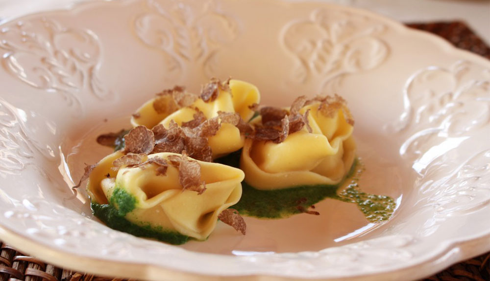 Close up of bowl with three pieces of pasta garnished with cured meats