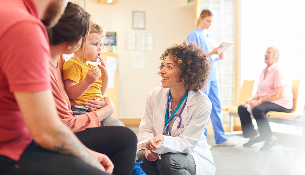 Doctor kneeling in waiting room to talk to seated patients