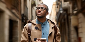 Man wearing glasses and holding his phone as he navigates his way through a foreign street