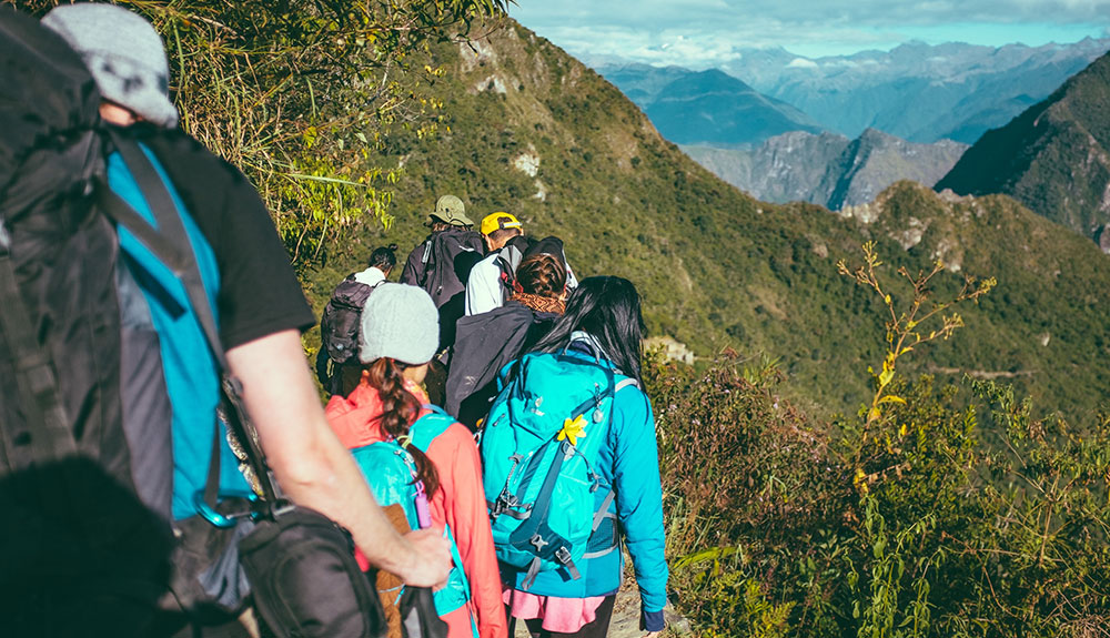Group of young adults hiking with backpacks on the side of a hill in the mountains