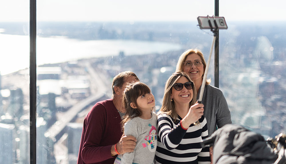 Man, two women and a child take a photo with their selfie stick from inside the CN Tower