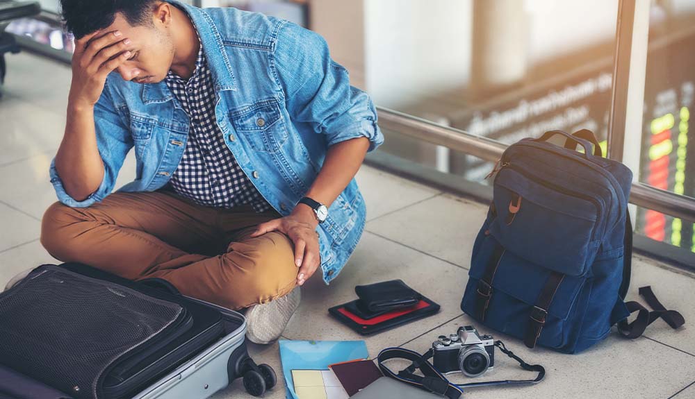 Man sitting on airport floor with backpack, camera and suitcase around him