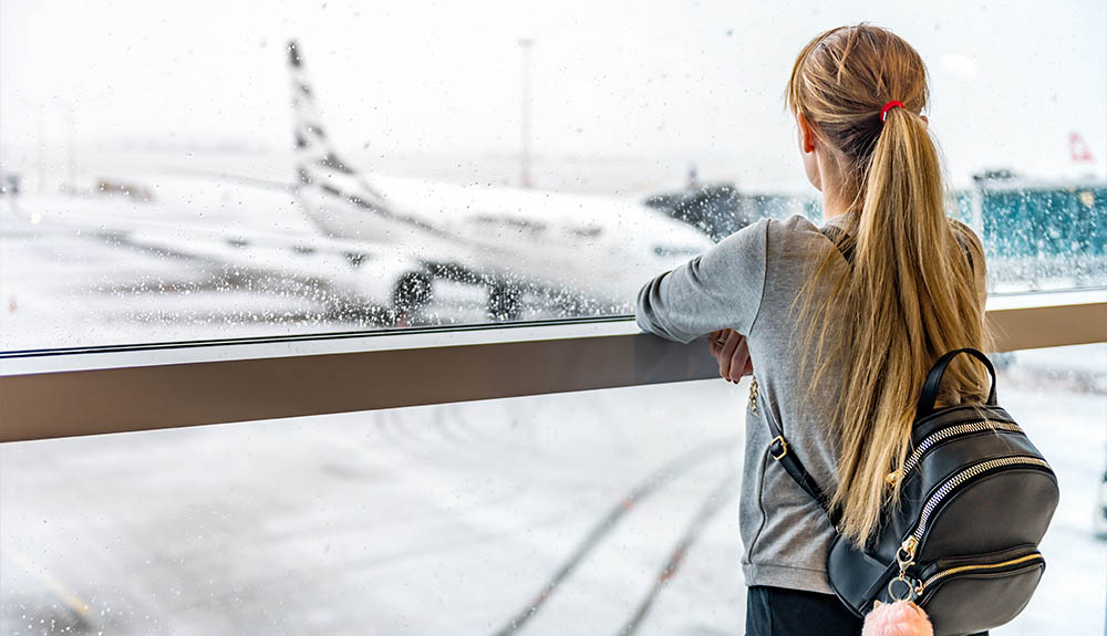 Woman with backpack standing at airport window watching the rain