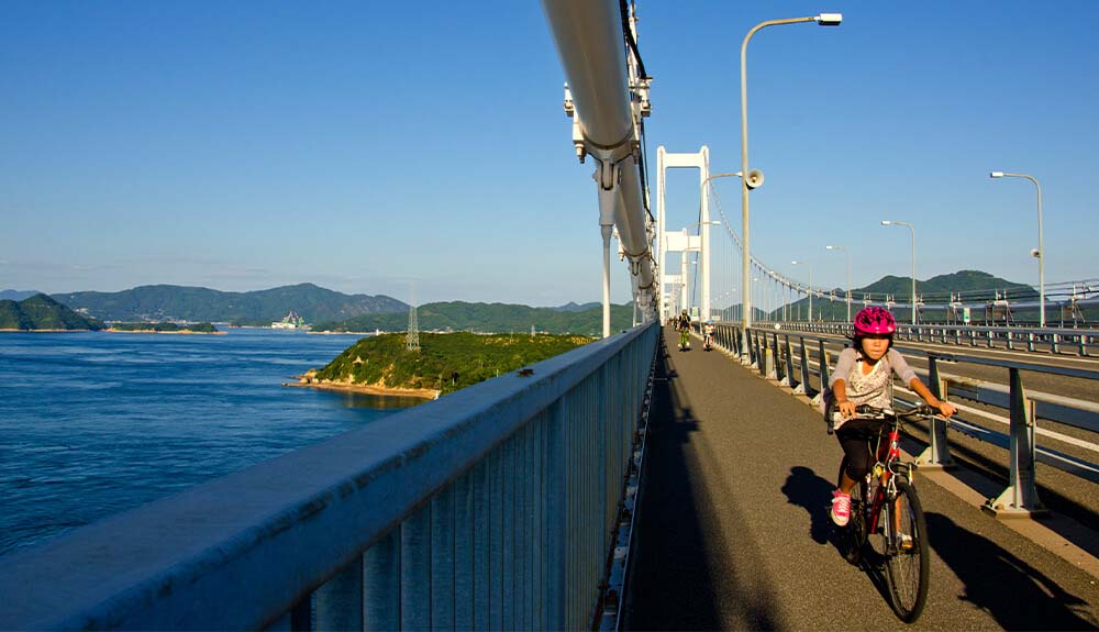 Cyclist riding across bridge over sea on the Shimanami Kaido cycle route in Japan