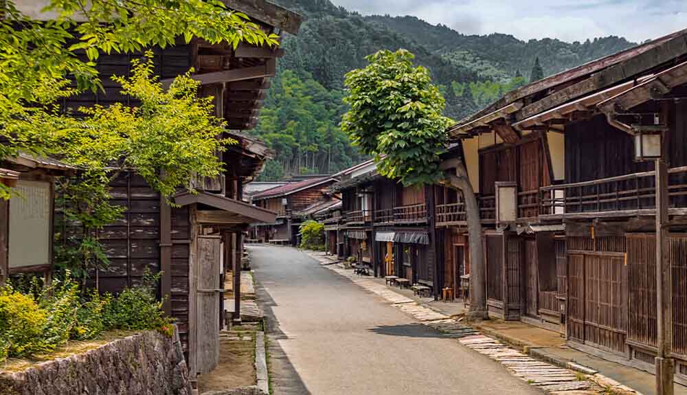 Street lined with traditional wooden buildings and background of green mountains along Japan's Nakasendo Way