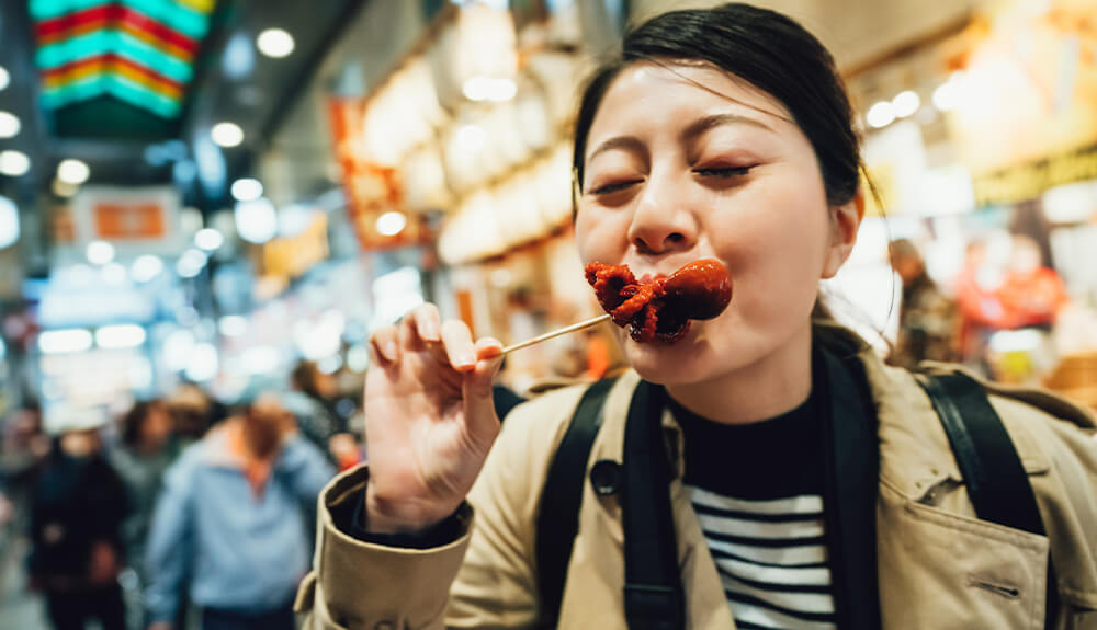 Woman eating tiny octopus off a skewer in the covered Nishiki Market in Kyoto, Japan