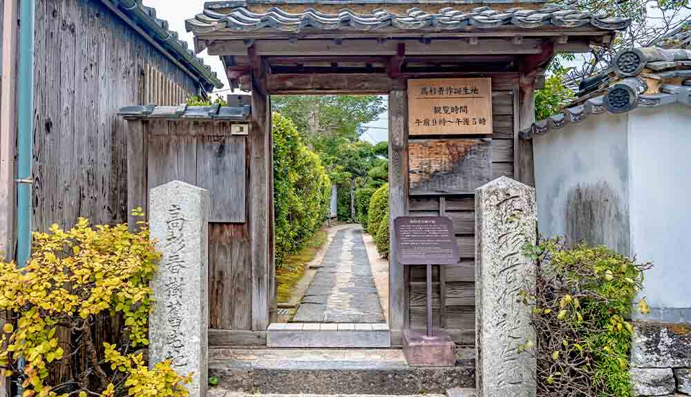 Weathered wooden gate with path leading into garden in Hagi, Japan