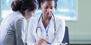 Doctor wearing a stethoscope points with a pen on a clipboard while talking to a woman 